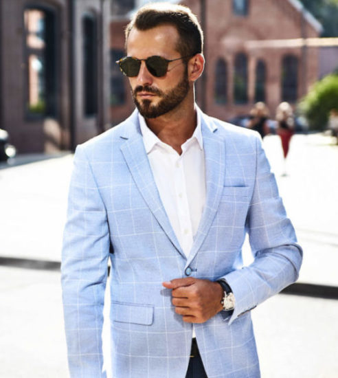 Portrait of sexy handsome fashion businessman model dressed in elegant blue suit posing on street background. Metrosexual