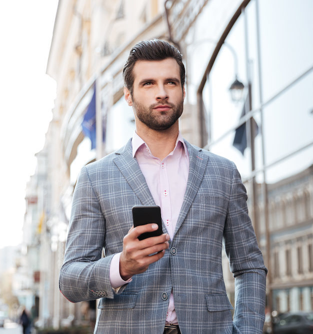 Handsome man in a jacket walking and holding mobile phone